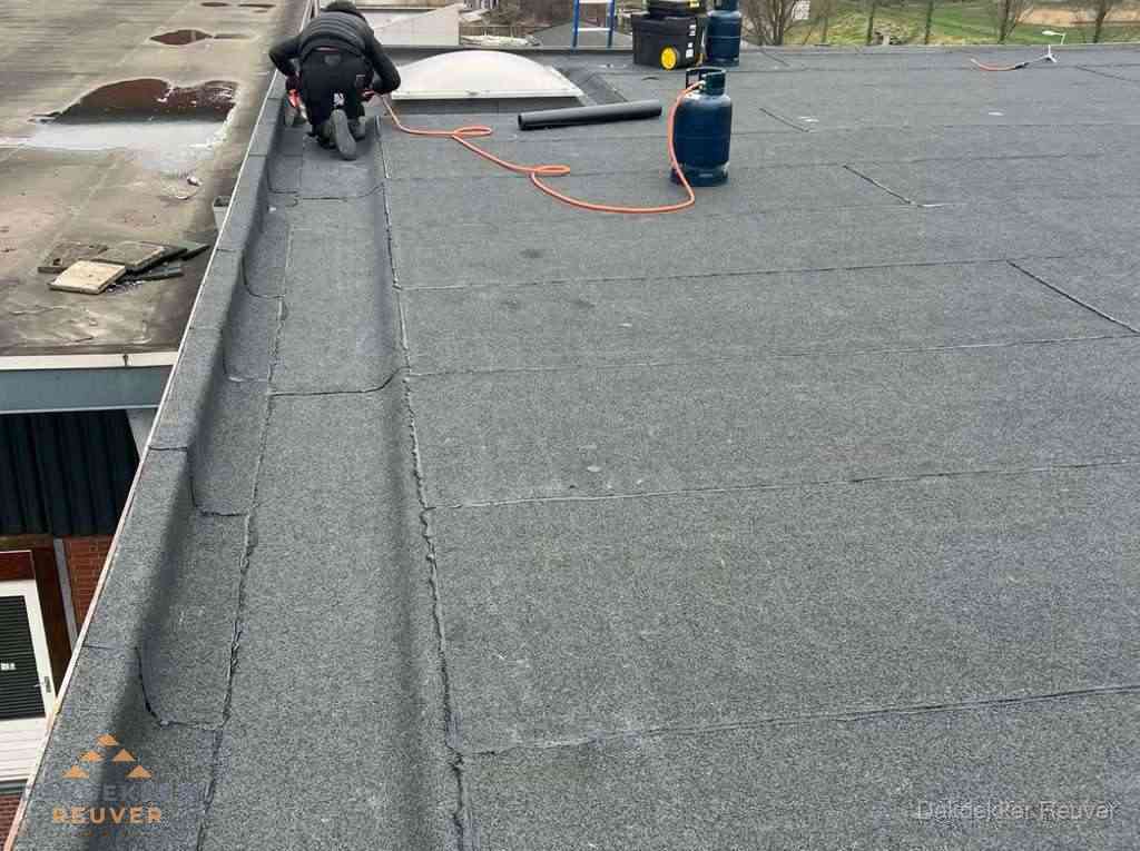 Dakdekker repareert bitumen dakbedekking op groot plat dak in Reuver